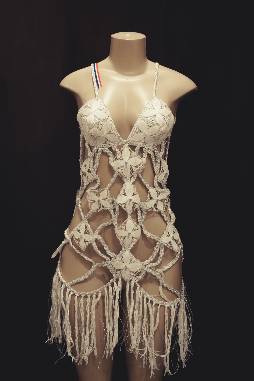Vestido blanco de ñanduti con flores tejidas y flecos, sobre un maniquí