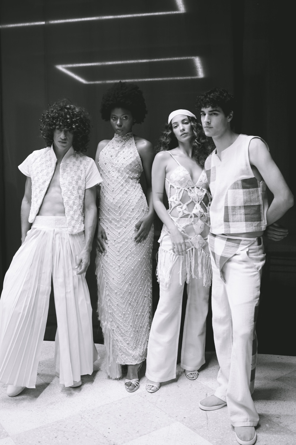 Cuatro modelos vestidos de blanco con prendas de encaje, lienzo plisado y ñanduti